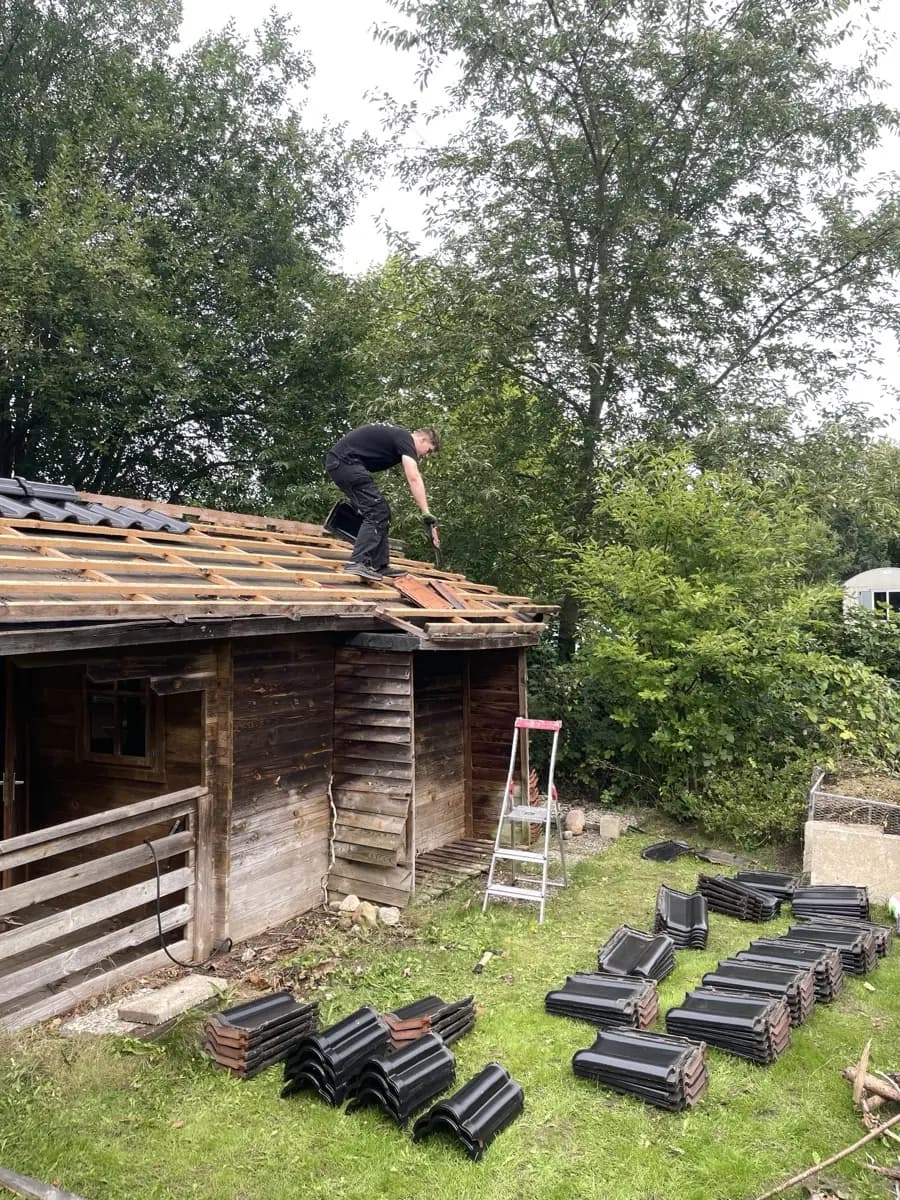 Holzgartenhaus in Reinbek beim Abdecken, ein Mitarbeiter steht auf dem Dach, die Dachlatten liegen frei