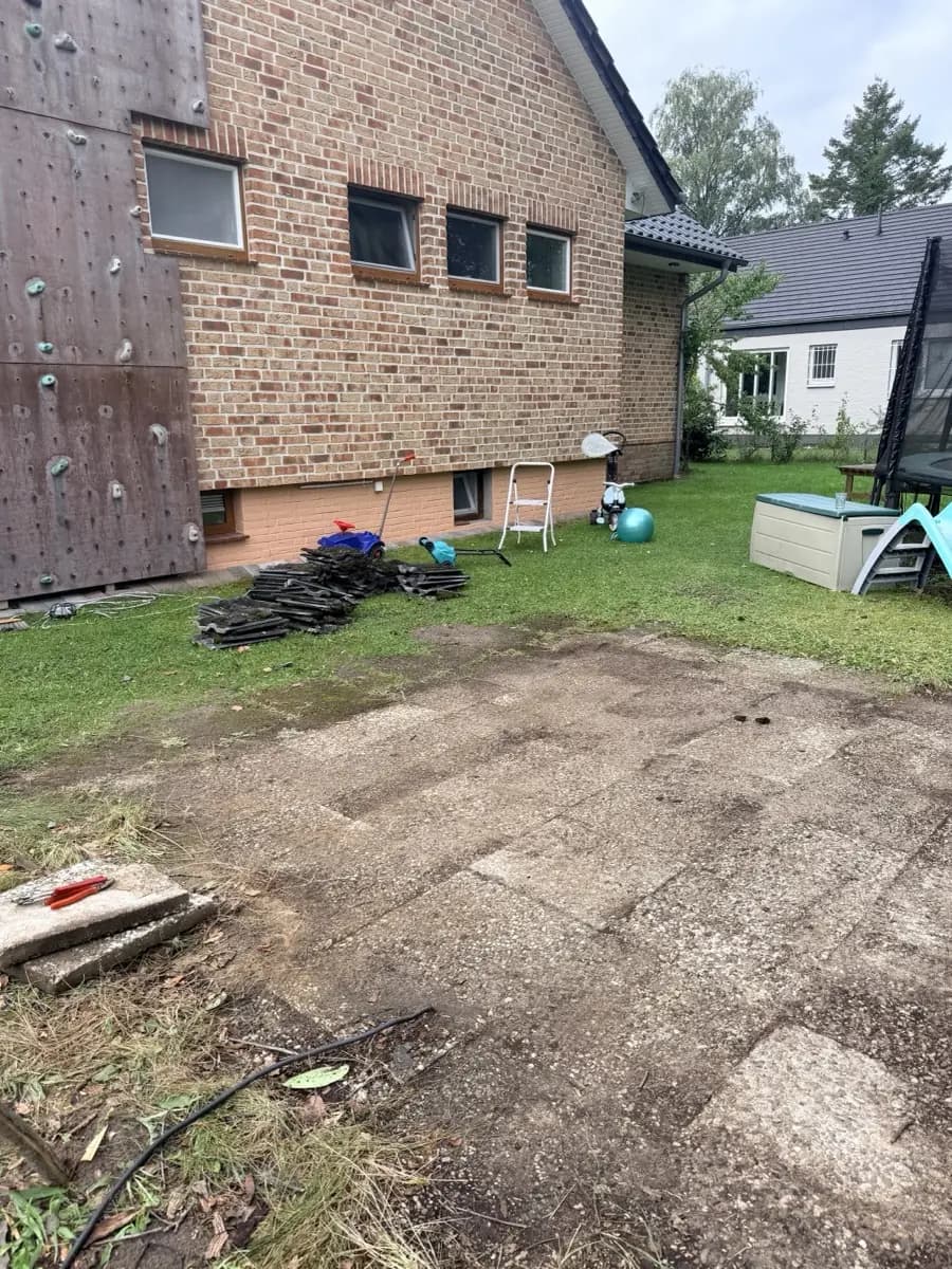 Hausgarten in Reinbek mit gestapeltem Rückbaumaterial auf dem Rasen, Klinkerhaus, Kletterwand und Spielbereich