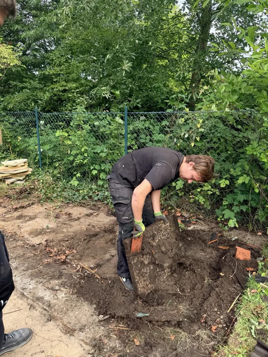 Mitarbeiter hebt eine Betonplatte des Fundaments von Hand aus dem Sandbett