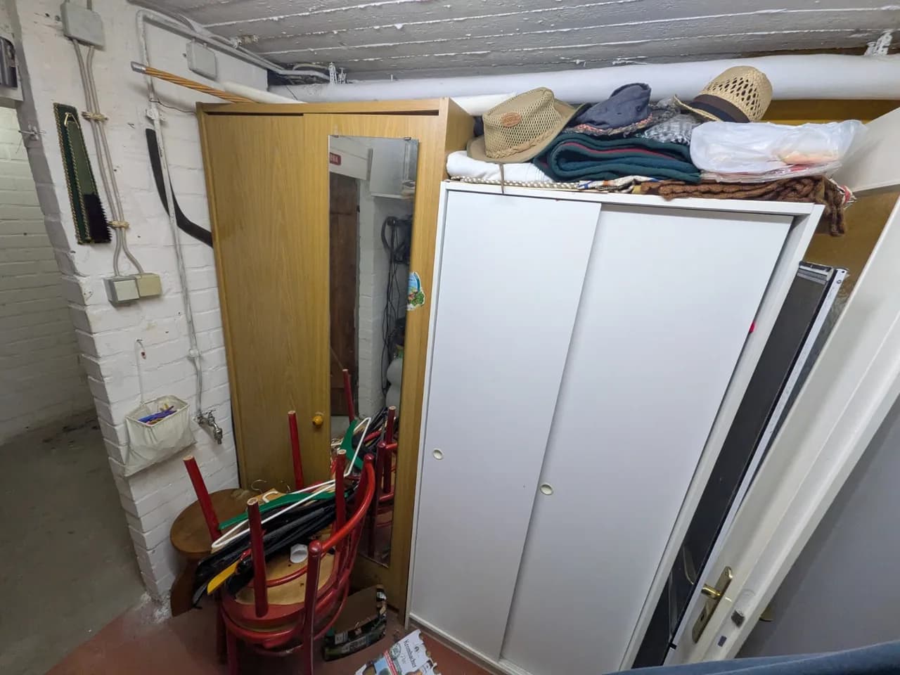 Zwei Kleiderschränke im Keller in Fuhlsbüttel vor der Räumung, davor gestapelte rote Holzstühle und Kleiderbügel