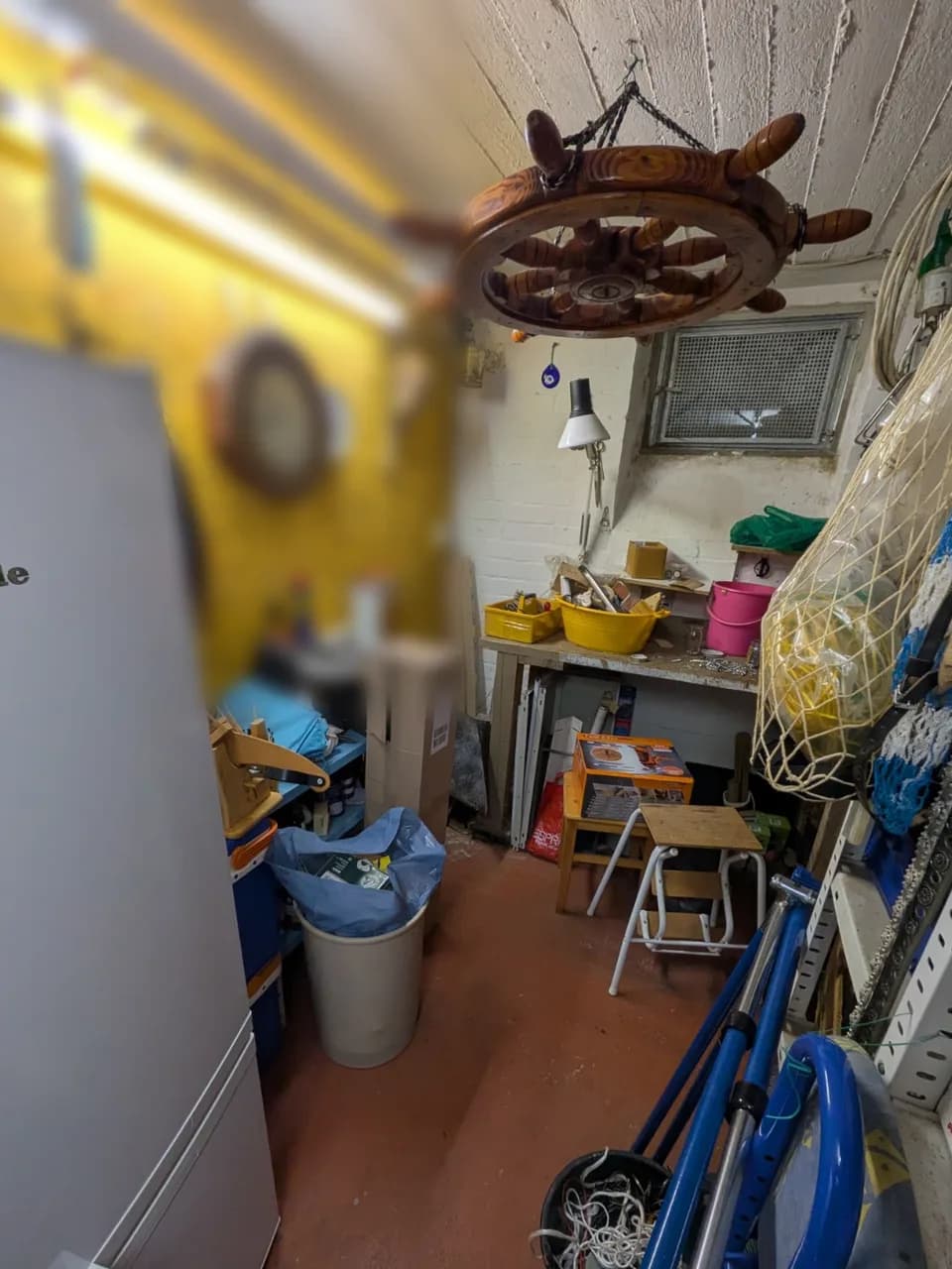 Kellerraum in Hamburg-Fuhlsbüttel vor der Räumung, Werkbank unter dem Kellerfenster, Steuerrad an der Decke, davor Eimer, Gestelle und Säcke