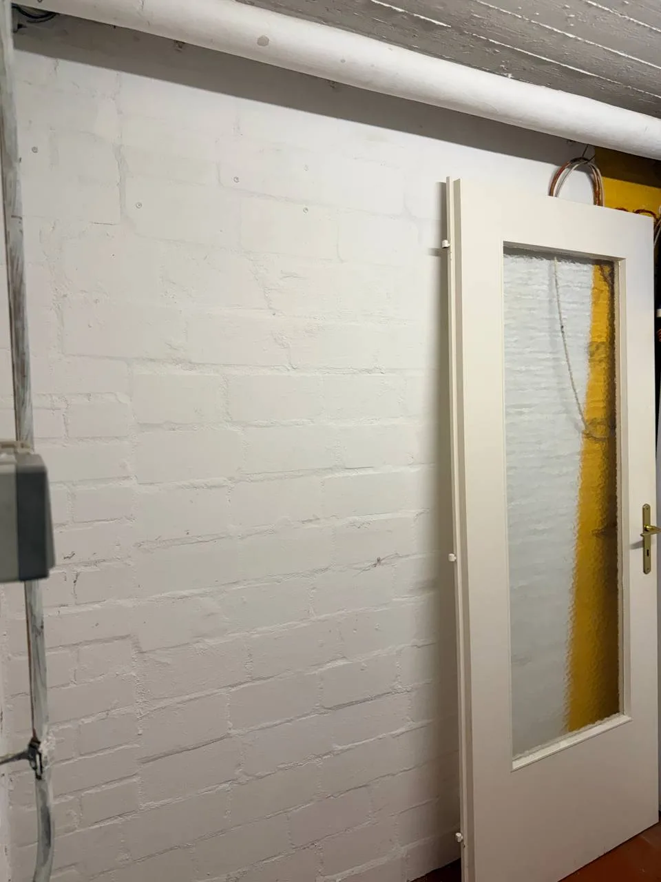 Weiß gestrichene Backsteinwand im Keller in Fuhlsbüttel nach der Räumung, daneben eine angelehnte Zimmertür