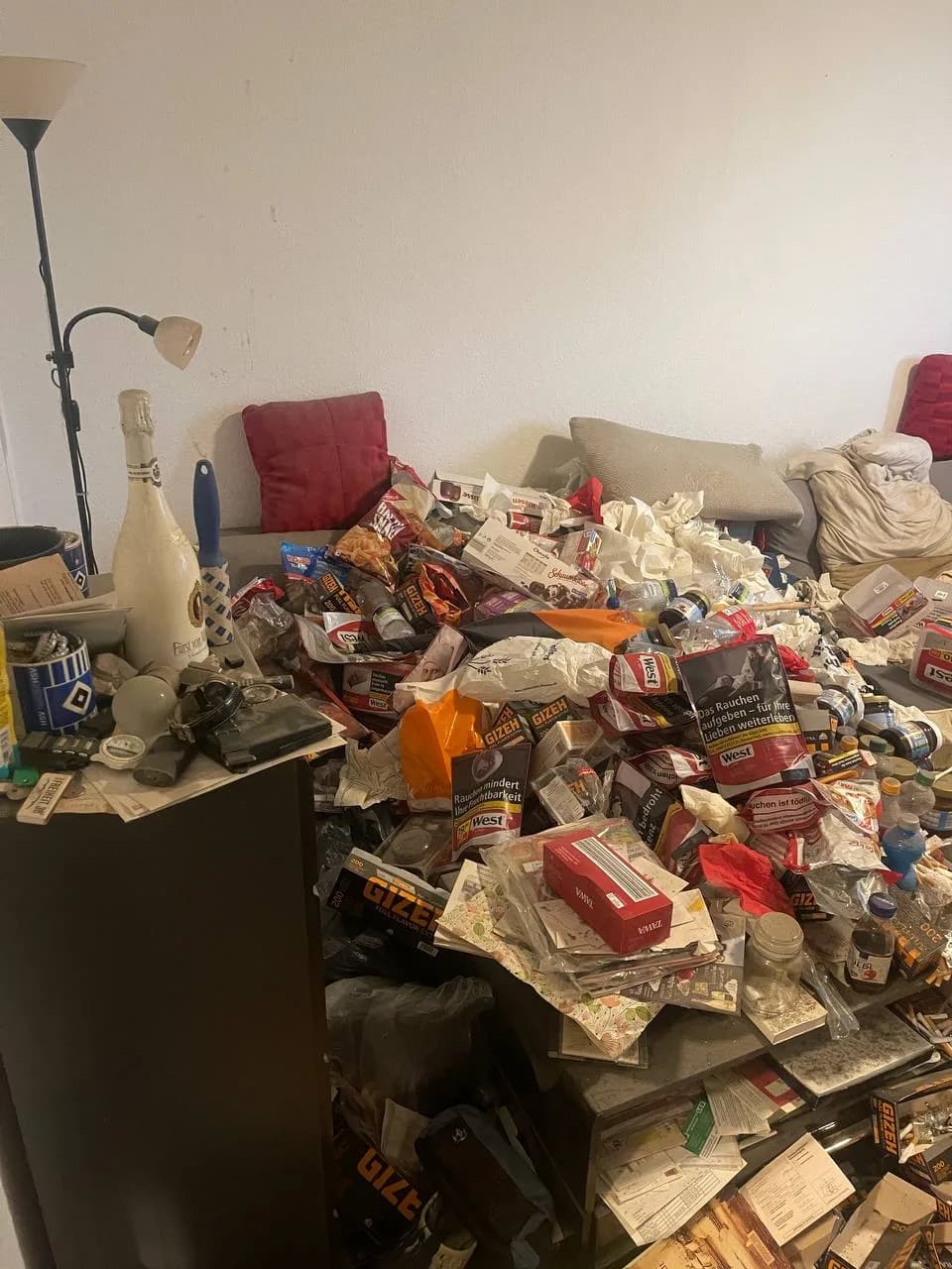 Vermülltes Wohnzimmer in Hamburg-Wandsbek, Sofa und Boden unter Verpackungsmüll und Tabakabfall