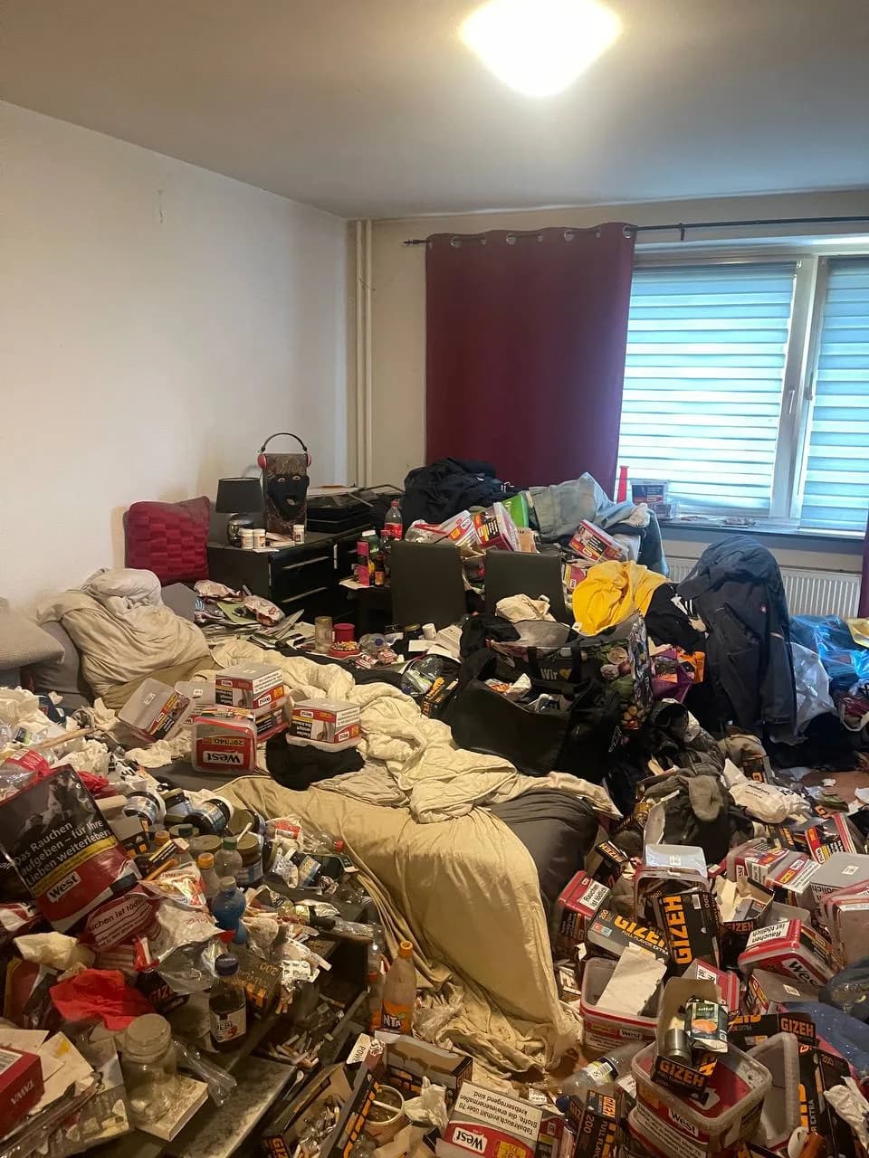 Übersicht des vermüllten Zimmers in Wandsbek mit Bett, Kleidung und Verpackungsmüll