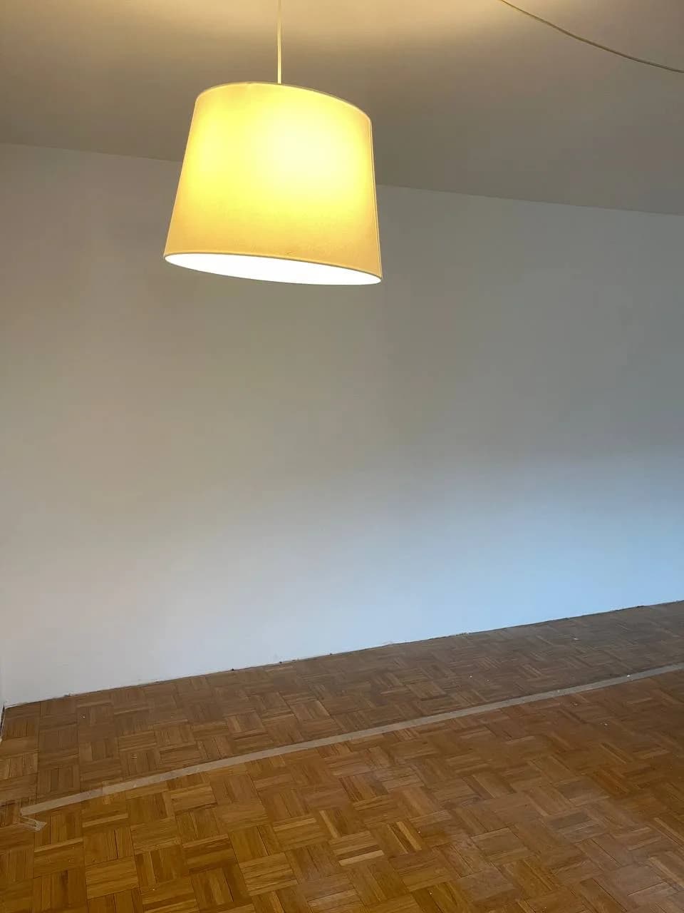 Leeres Zimmer in Wedel nach der Auflösung mit freigelegtem Stabparkett und Pendelleuchte