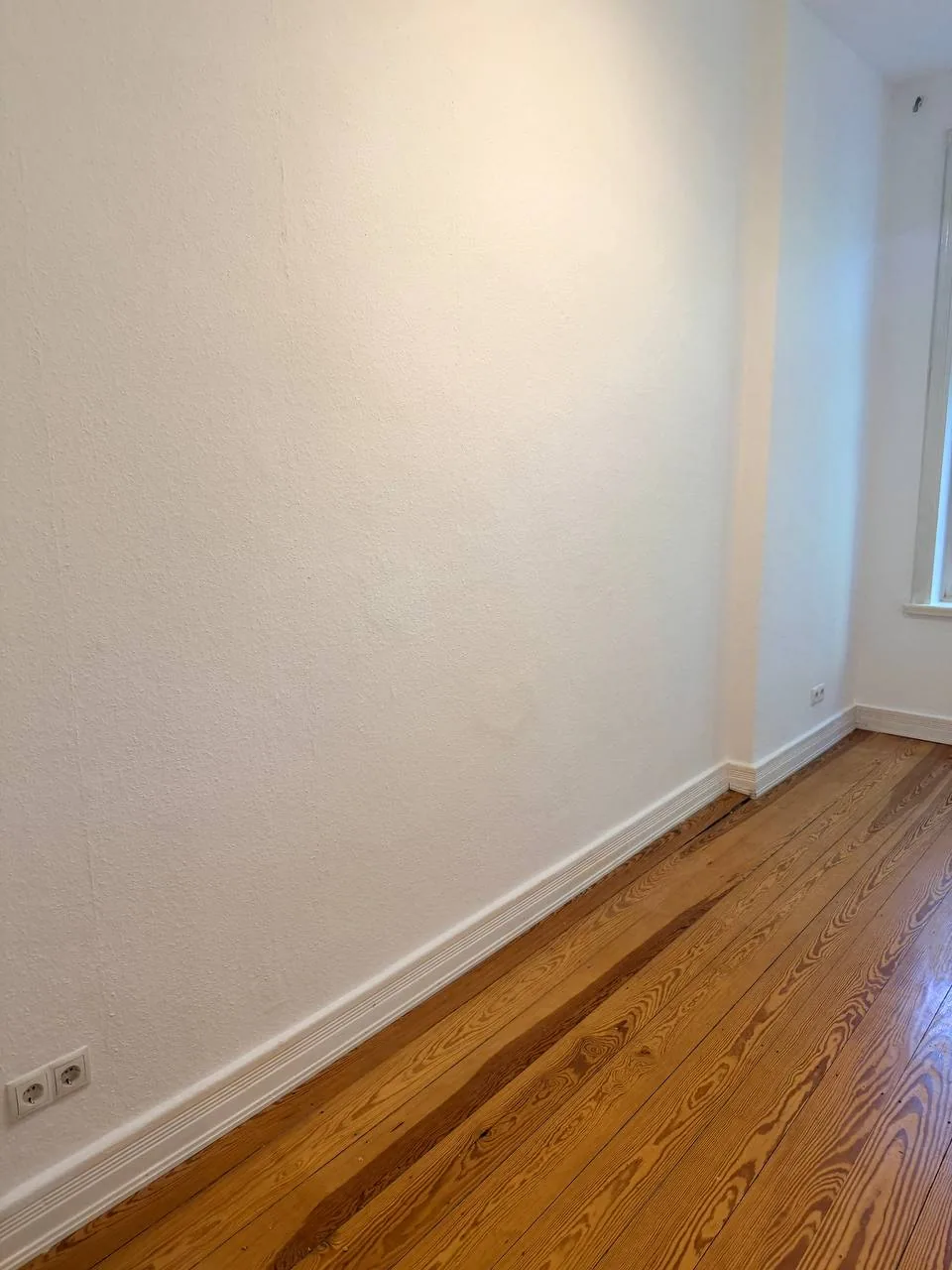 Detail von abgeschliffenen Kiefer-Dielen und neuen weißen Sockelleisten in einem Hamburger Altbau