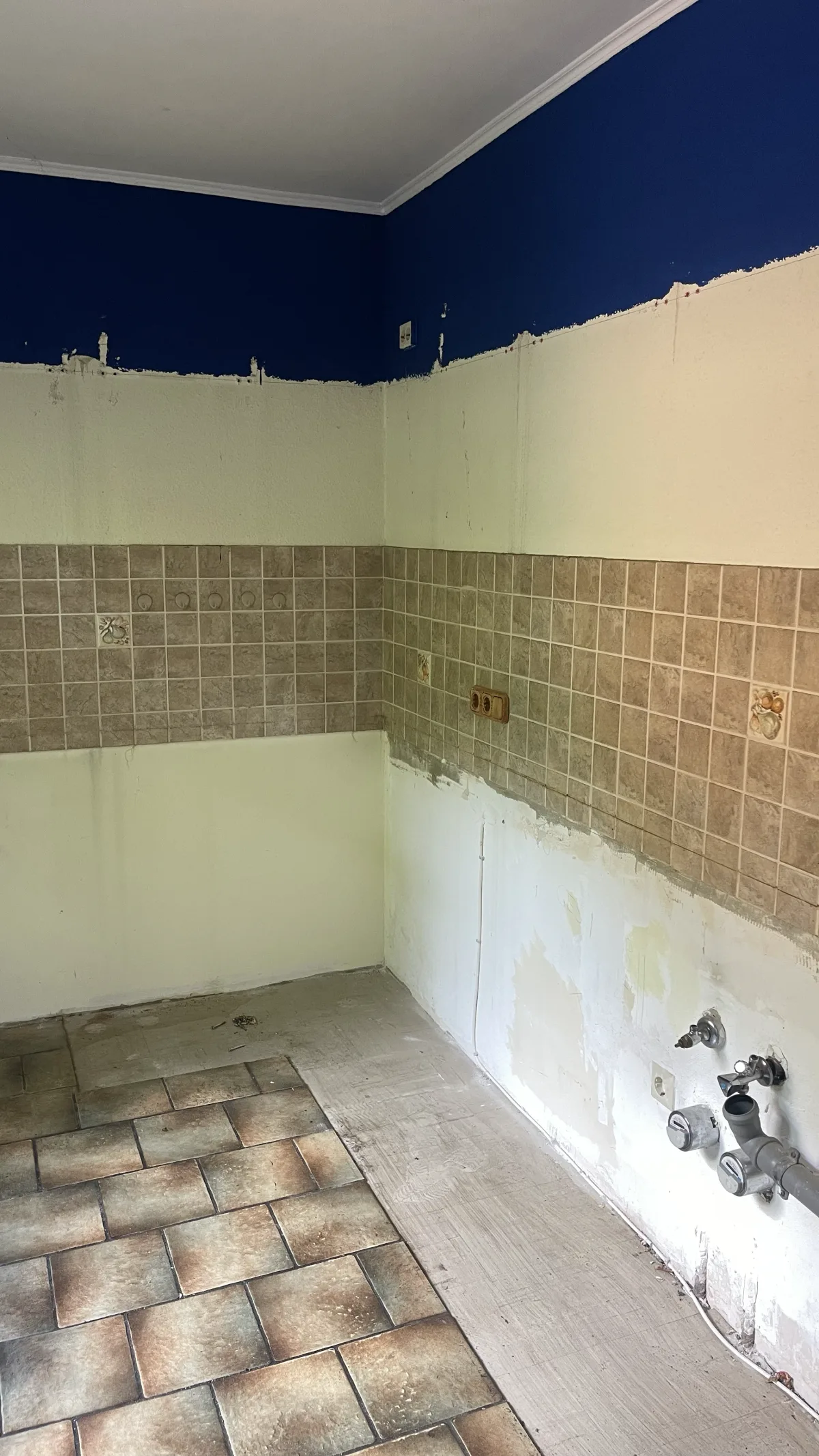 Freigelegte Wand mit altem Fliesenspiegel und sichtbaren Wasser- und Abflussanschlüssen nach dem Küchenausbau