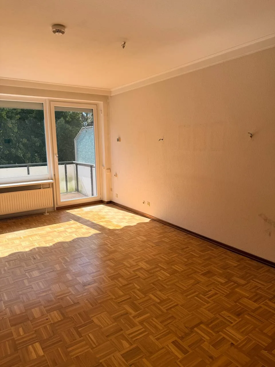 Leeres Wohnzimmer in Hamburg-Wandsbek nach der Räumung mit Mosaikparkett und Balkontür